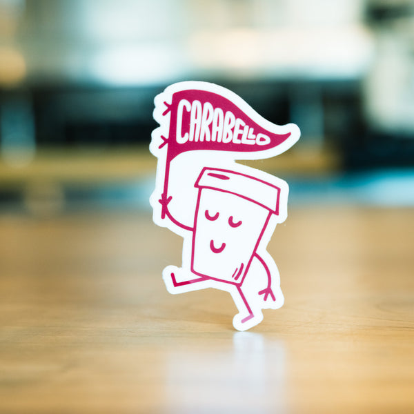 A sticker featuring a cartoon coffee cup with arms and legs holding a banner that says Carabello