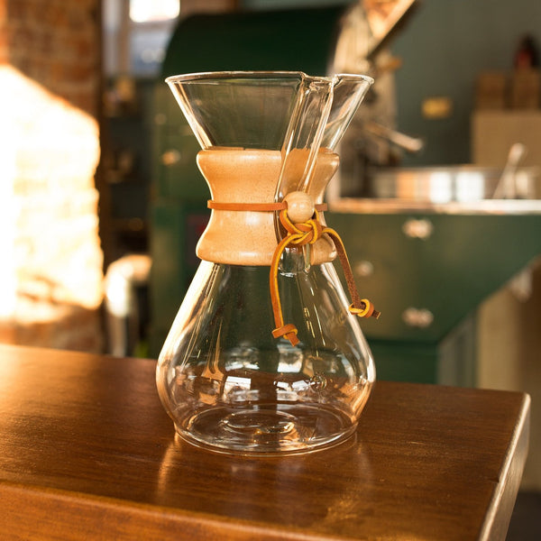 Glass chemex coffee brewer with a wooden collar and a leather strap around it.  