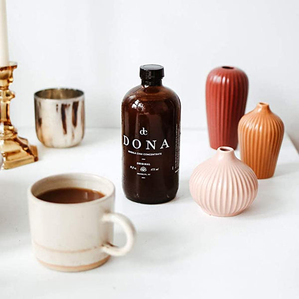Brown glass bottle of Dona Chai concentrate with a mug of chai