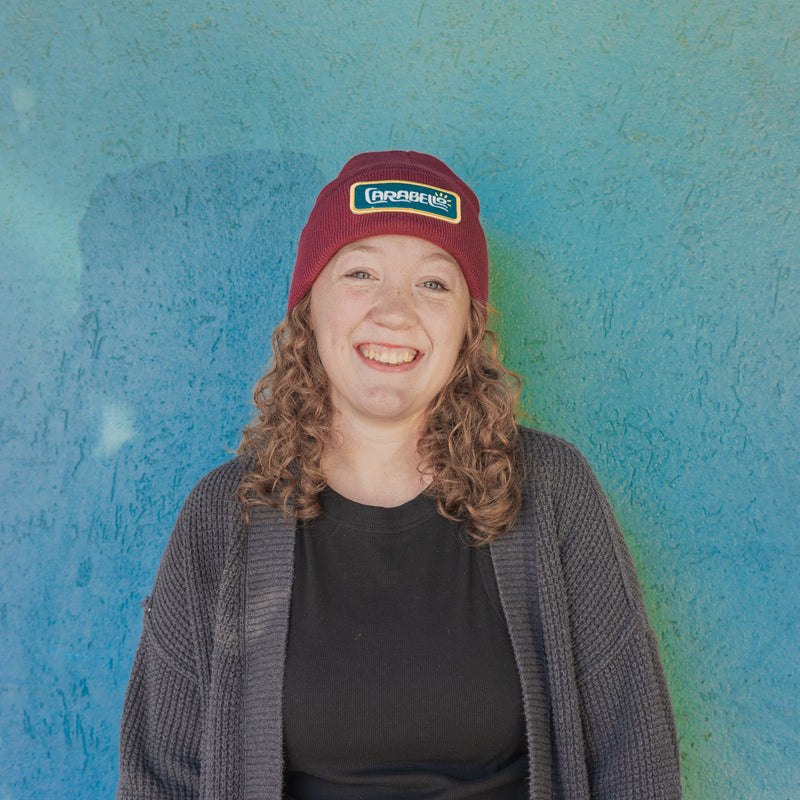 Person wearing a maroon cap with a logo against a blue textured wall
