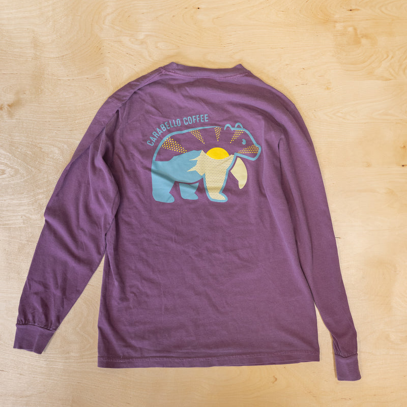 Purple long-sleeve shirt with a bear graphic and text on a wooden surface