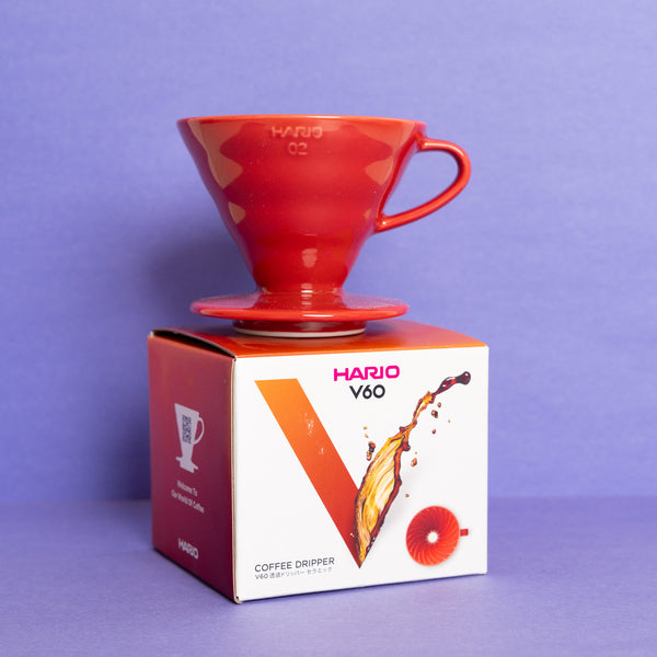 Red Hario coffee dripper on top of its packaging box against a purple background