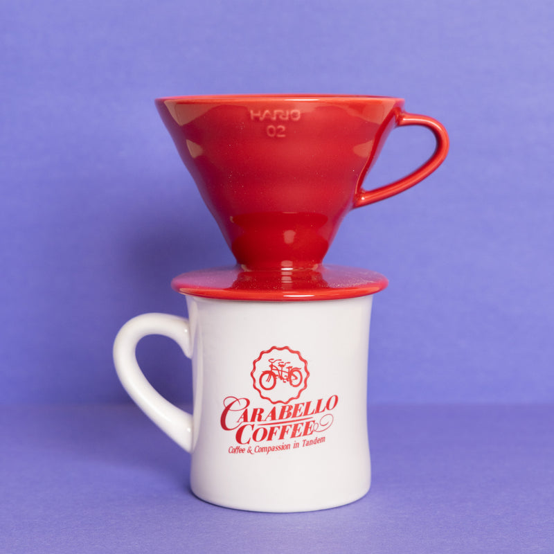 Red coffee brewer on a white mug with 'Carabello Coffee' branding against a purple background