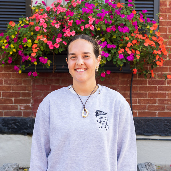 Person wearing a gray sweatshirt with a graphic design, standing in front of a brick wall with colorful flowers.