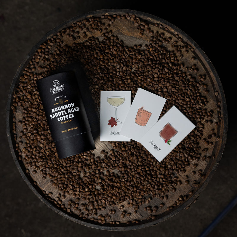 Bourbon barrel aged coffee package on a bed of coffee beans with cocktail illustrations.