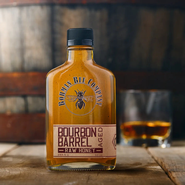 Bottle of Bourbon Bee Company bourbon barrel aged raw honey with a glass in the background.