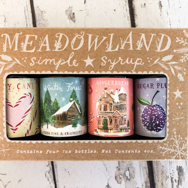 A box containing four bottles of Meadowland Simple Syrup in different holiday flavors, including Winter Forest, Gingerbread, Sugar Plum, and Candy Cane.
