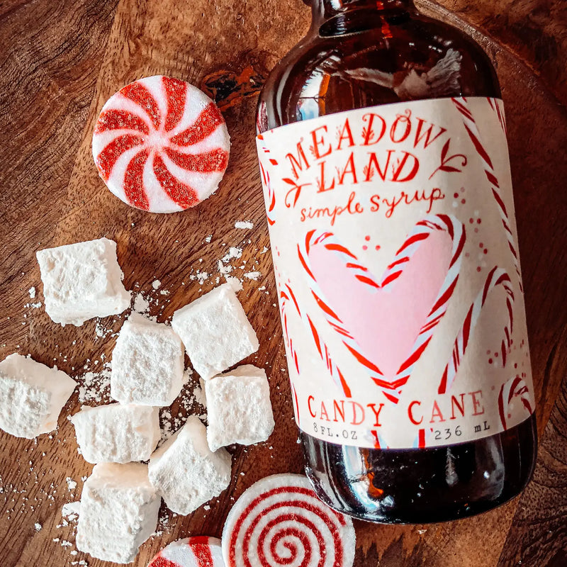 Bottle of Meadowland Candy Cane simple syrup with candy canes and marshmallows on a wooden surface