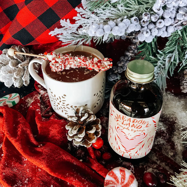 Hot chocolate with peppermint stick, bottle of Meadowland syrup, and Christmas decorations.