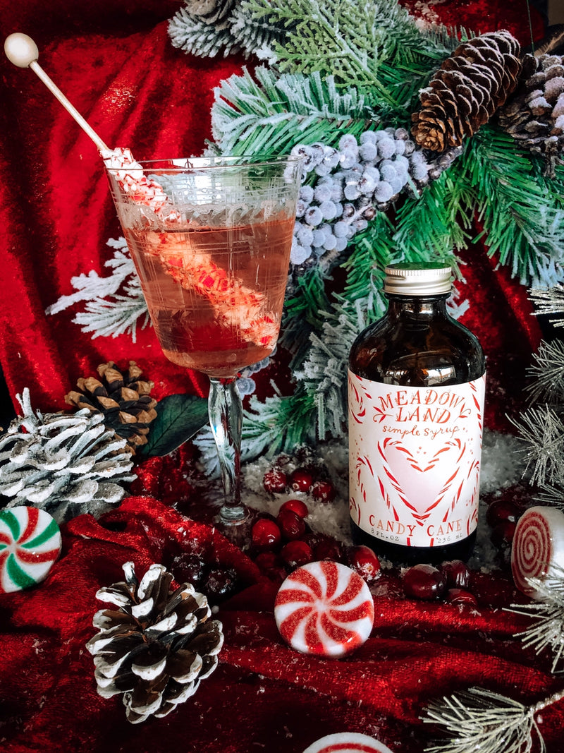 Christmas-themed cocktail setup with a bottle of 'Meathook Land Candy Cane' syrup.