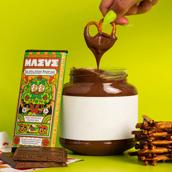 Maeve Nutbutter Pretzel chocolate bar being dipped into a jar of chocolate spread with pretzels on a green background.