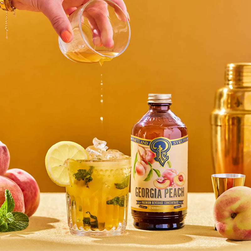 cocktail with hand pouring peach syrup into it 