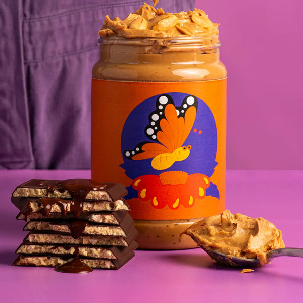 Jar of peanut butter with butterfly design, chocolate bars, and a spoonful of peanut butter on a purple background