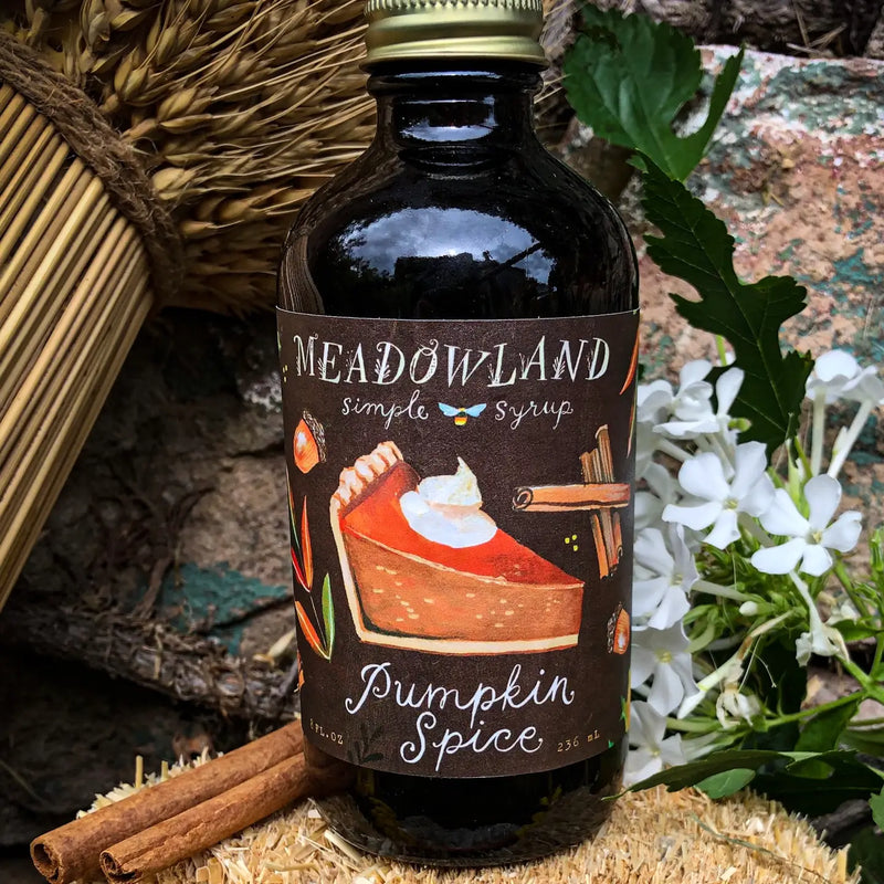 Bottle of Meadowland Pumpkin Spice simple syrup with a label featuring a pie illustration, surrounded by cinnamon sticks and flowers.