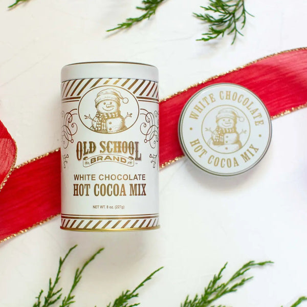 Old School Brand white chocolate hot cocoa mix can with a red ribbon on a white background with greenery.