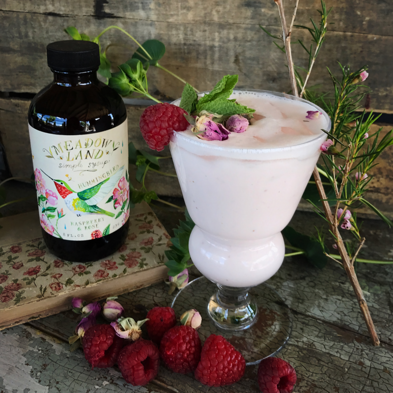 Meadowland Brand Syrup in Raspberry and Rose  in a 8 oz bottle.  Next to a cocktail with raspberry and rose on it.  
